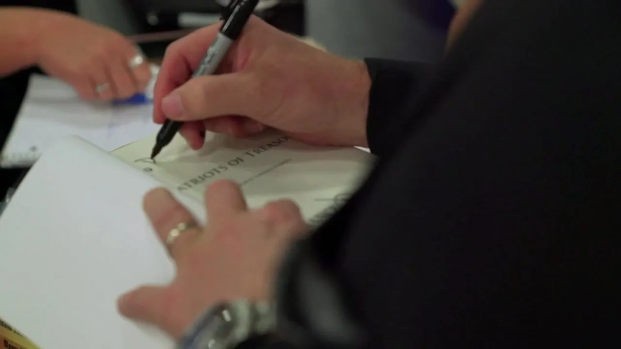 A hand signing the title page of a book